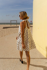 Robe à pois col montant portée par une femme, silhouette entière, plage, mur jaune