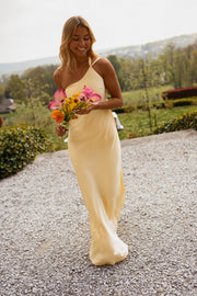 Robe longue effet soie jaune portée par une femme, vue de trois-quarts, bouquet rose, gravier
