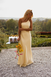 Robe longue effet soie jaune portée par une femme, silhouette entière, bouquet, gravier