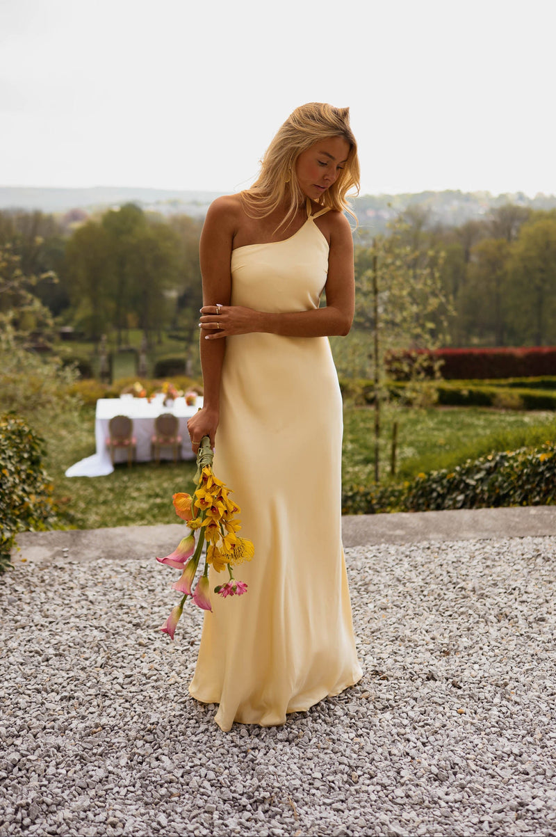 Robe longue effet soie jaune portée par une femme, silhouette entière, bouquet, gravier