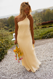 Robe longue effet soie jaune portée par une femme, vue de trois-quarts, bouquet jaune, gravier