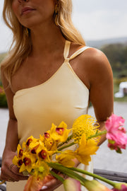 Robe longue effet soie jaune portée par une femme, vue rapprochée, bouquet de fleurs jaunes, bretelle