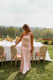 Robe longue fluide effet soie portée par une femme, silhouette entière, tables dressées, chaises dorées