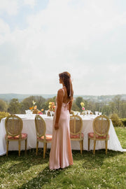Robe longue fluide effet soie portée par une femme, vue de profil, chaises dorées, jardin