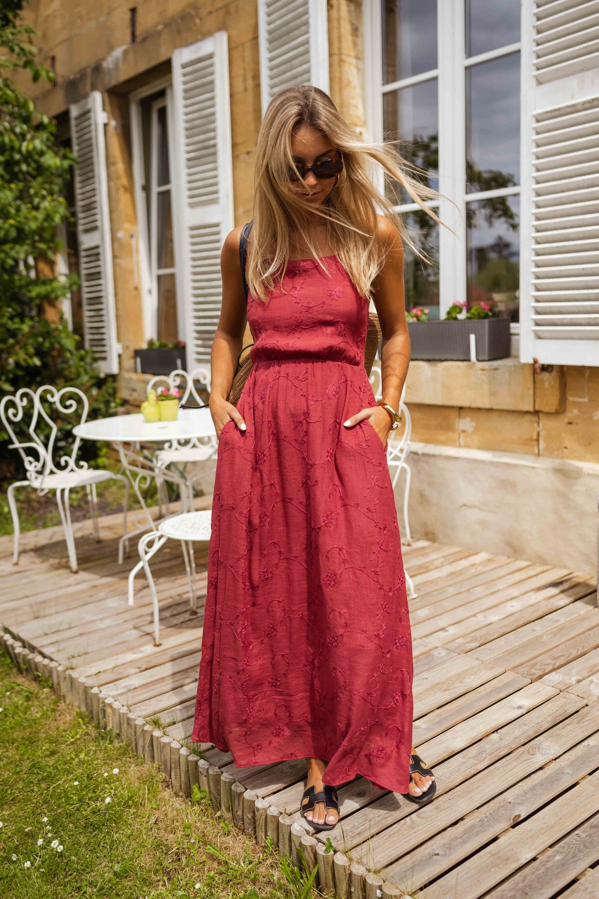 Robe brodée à col carré portée par une femme, silhouette entière, terrasse en bois, table
