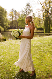 Robe brodée à bretelles ajustables portée par une femme, vue de face, bouquet d'hortensias, pelouse