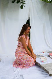Robe fleurie longue à volants portée par une femme, assise sur le drap blanc