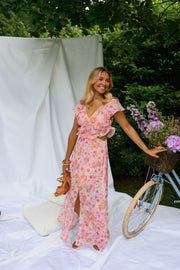 Robe fleurie longue à volants portée par une femme, silhouette entière, vélo, sandales à la main