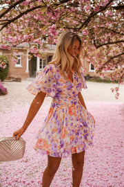 Robe courte fleurie cache-cœur portée par une femme, en marchant, pétales roses, pochette