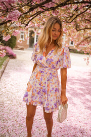 Robe courte fleurie cache-cœur portée par une femme, silhouette entière, cerisiers en fleurs, pochette
