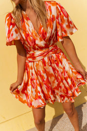 Robe cache-cœur fluide rose et orange portée par une femme, vue rapprochée, décolleté croisé, manches