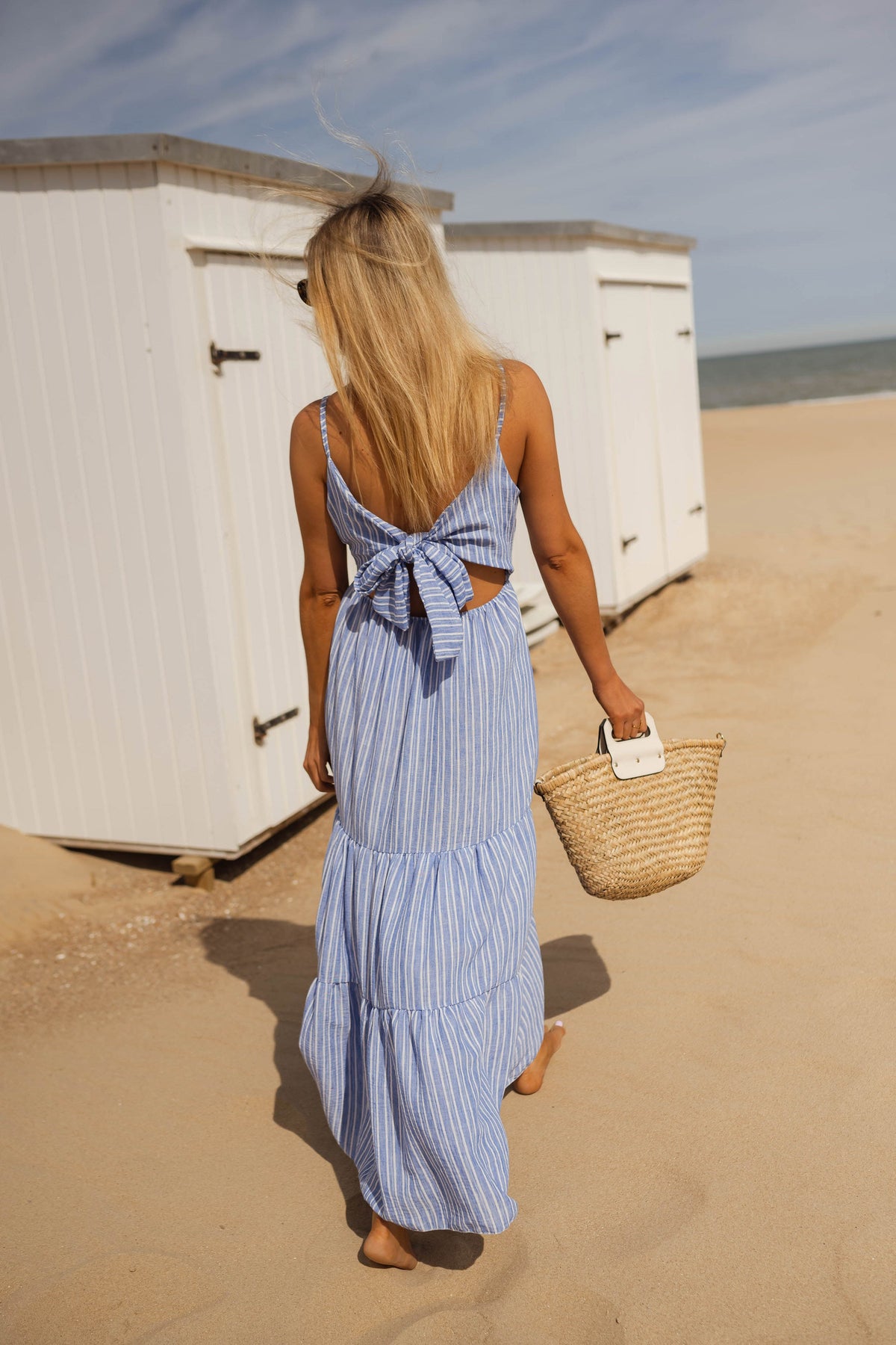Robe longue rayée à bretelles portée par une femme, vue de dos, cabines, panier de paille