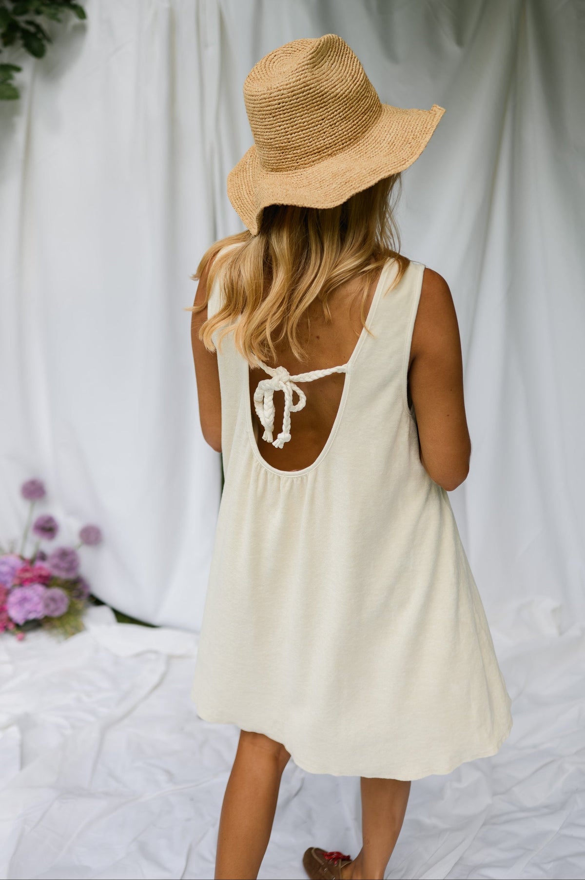 Robe éponge à dos ouvert portée par une femme, vue de dos, chapeau de paille, drapés blancs