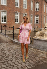 Robe à volants col V portée par une femme, vue de face, bâtiment en brique, grille