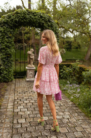 Robe à volants col V portée par une femme, vue de face, tonnelle de verdure, sac violet