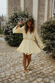 Robe courte à manches évasées portée par une femme, silhouette entière, buissons, jupe qui vole