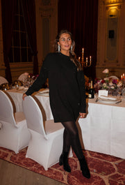Robe pull brillante portée par une femme, silhouette entière, chaises blanches, collants