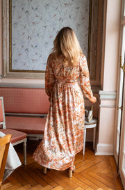 Robe longue fluide col V portée par une femme, vue de dos, parquet, fauteuils roses