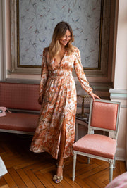 Robe longue fluide col V portée par une femme, silhouette entière, fauteuil rose, parquet