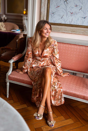 Robe longue fluide col V portée par une femme, assise, banc rose, parquet