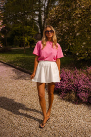 Short taille haute élastiqué blanc porté par une femme, silhouette entière, allée, massif de fleurs mauves