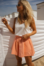 Short taille haute élastiqué orange porté par une femme, vue de trois-quarts, cabines blanches, main dans les cheveux