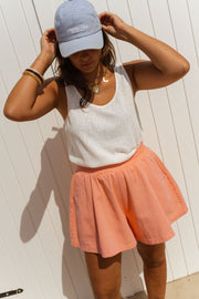 Short taille haute élastiqué orange porté par une femme, vue rapprochée, casquette, short rose