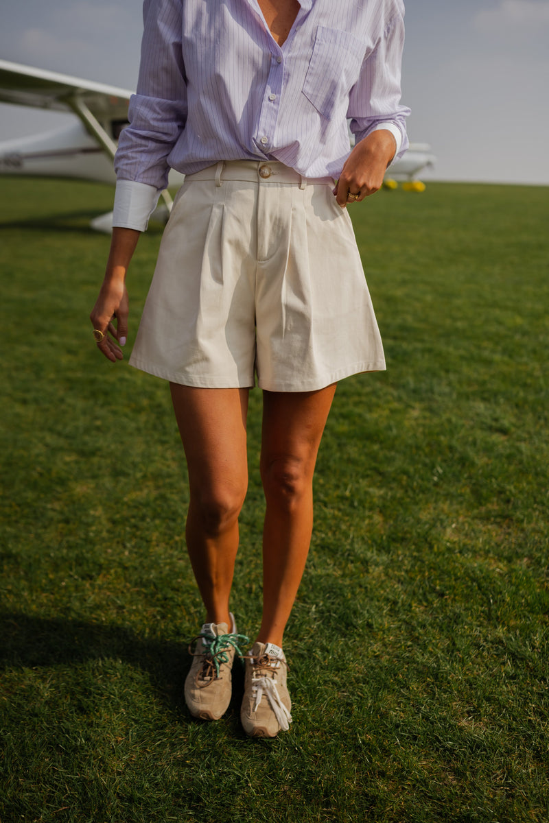 Short taille haute à poches porté par une femme, silhouette entière, pelouse, chemise lavande