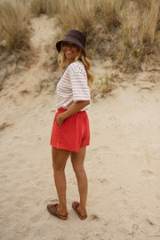 Short en coton effet délavé porté par une femme, vue de trois-quarts, dunes, main au chapeau