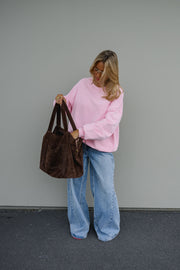 Sweat ample col rond porté par une femme, silhouette entière, sac marron à la main, cheveux longs, devant un mur gris