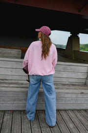 Sweat ample col rond porté par une femme, vue de dos, casquette rose, jean large, banc en bois