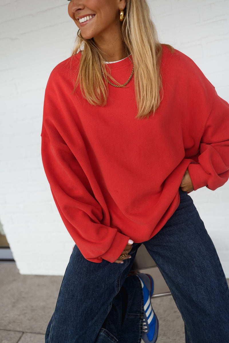 Sweat ample à col rond porté par une femme, vue de trois-quarts, mur blanc, cheveux blonds