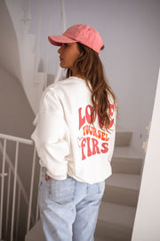 Sweat à col rond blanc porté par une femme, vue de dos, casquette rose, inscription rouge
