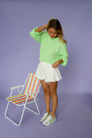 T-shirt rayé ample manches longues porté par une femme, silhouette entière, près d'une chaise de plage, main sur la tête