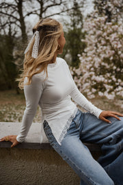 T-shirt moulant à dentelle asymétrique porté par une femme, assise, sur un muret, vue de trois-quarts