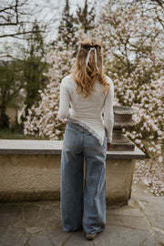 T-shirt moulant à dentelle asymétrique porté par une femme, vue de dos, jean, sur un muret
