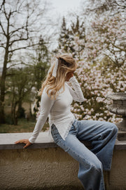T-shirt moulant à dentelle asymétrique porté par une femme, assise, sur un muret, jean