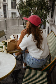 T-shirt blanc à cœur vichy bleu porté par une femme, vue de dos, casquette rose, à une table