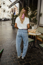 T-shirt blanc à cœur vichy rouge porté par une femme, silhouette entière, jean clair, rue, nœud rose dans les cheveux