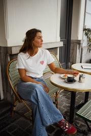 T-shirt blanc à cœur vichy rouge porté par une femme, assise, à une table, café