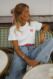 T-shirt blanc à cœur vichy rouge porté par une femme, assise, chaise verte, jean clair, ceinture rouge