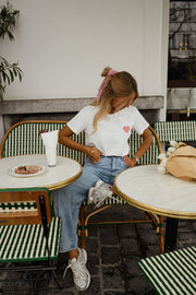 T-shirt blanc à cœur vichy rouge porté par une femme, assise, à une table, baskets