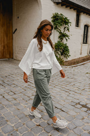 T-shirt resserré à la taille porté par une femme, en marchant, pantalon vert-gris, sur des pavés