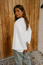 T-shirt resserré à la taille porté par une femme, vue de dos, pantalon vert-gris, devant un mur en bois