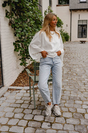 T-shirt resserré à la taille porté par une femme, silhouette entière, jean clair, sur des pavés