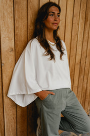T-shirt resserré à la taille porté par une femme, vue rapprochée, adossée à un mur en bois, main dans la poche