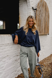 T-shirt à manches chauve-souris porté par une femme, silhouette entière, sac à main, pantalon vert-gris