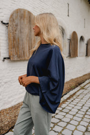 T-shirt à manches chauve-souris porté par une femme, vue de trois-quarts, manches chauve-souris, sur des pavés
