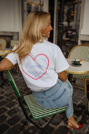 T-shirt à logo cœur dos porté par une femme, assise, logo cœur rose dans le dos, chaise verte