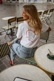 T-shirt à logo cœur dos porté par une femme, assise, logo cœur dans le dos, à une table